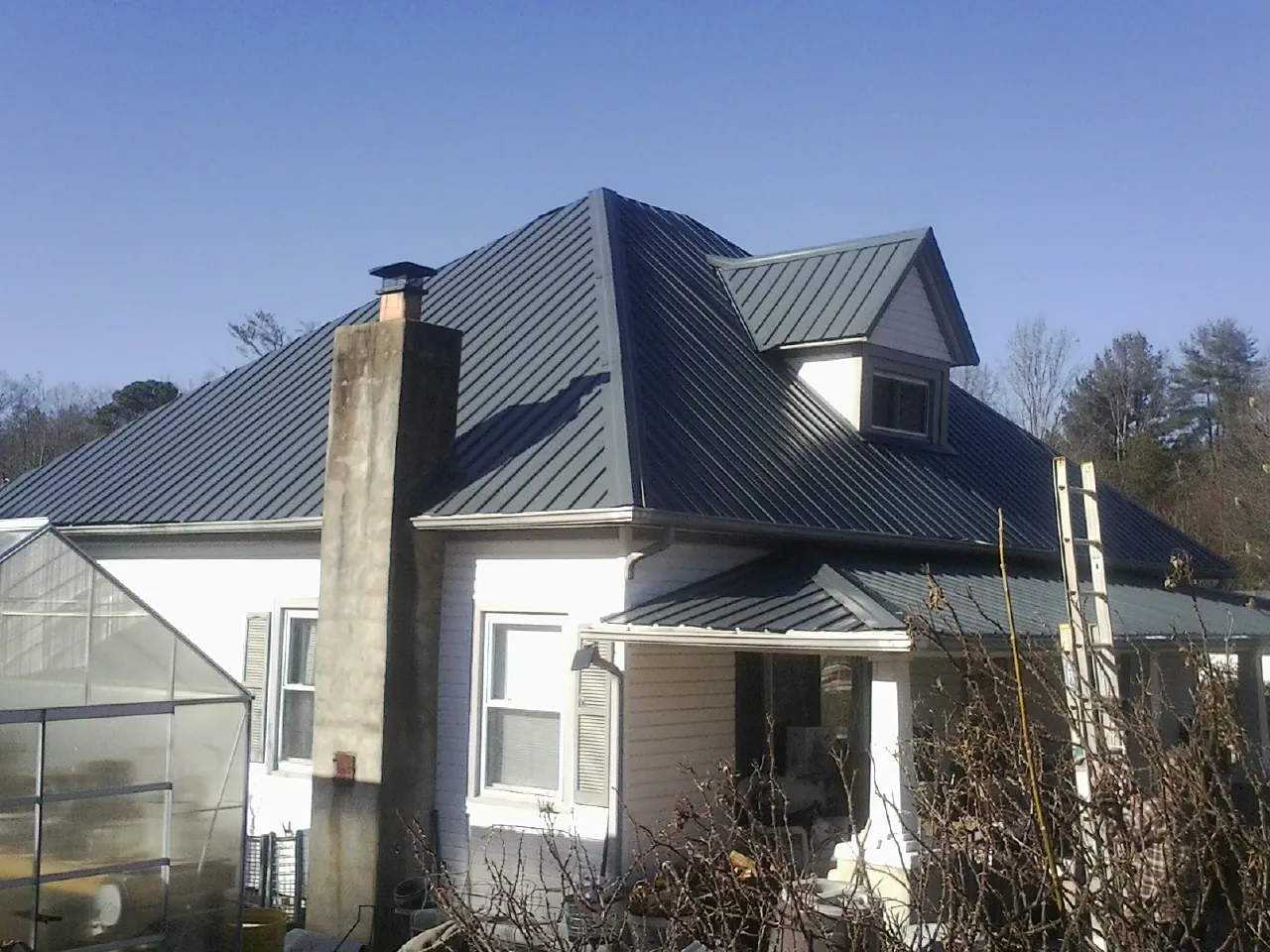 Dark blue standing seam metal roof on a white farmhouse with dormer — Slate & Tile Roof Repair by Roofing Brothers in Horace