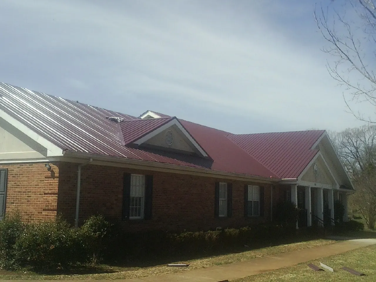 Red metal roof with gabled entries on a long brick building, from a Hail Damage Roof Repair job in Horace