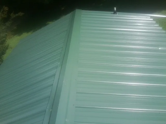 New green metal panels meeting at the ridge of a roof — Flat Roof Repair work by our crew in Horace