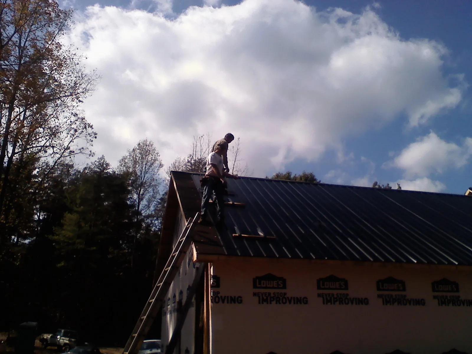 Roofer fastening dark metal panels high against a cloudy sky, from a Roof Inspection job in Horace