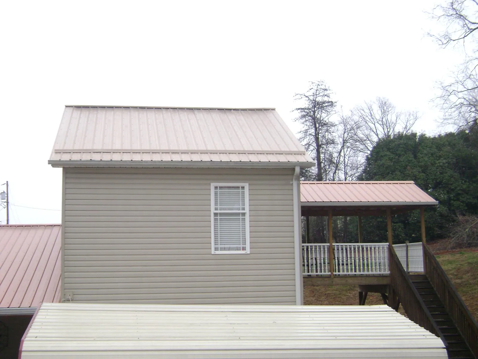 Tan metal roofs on a two story addition and attached porch, from a Roof Replacement job in Horace